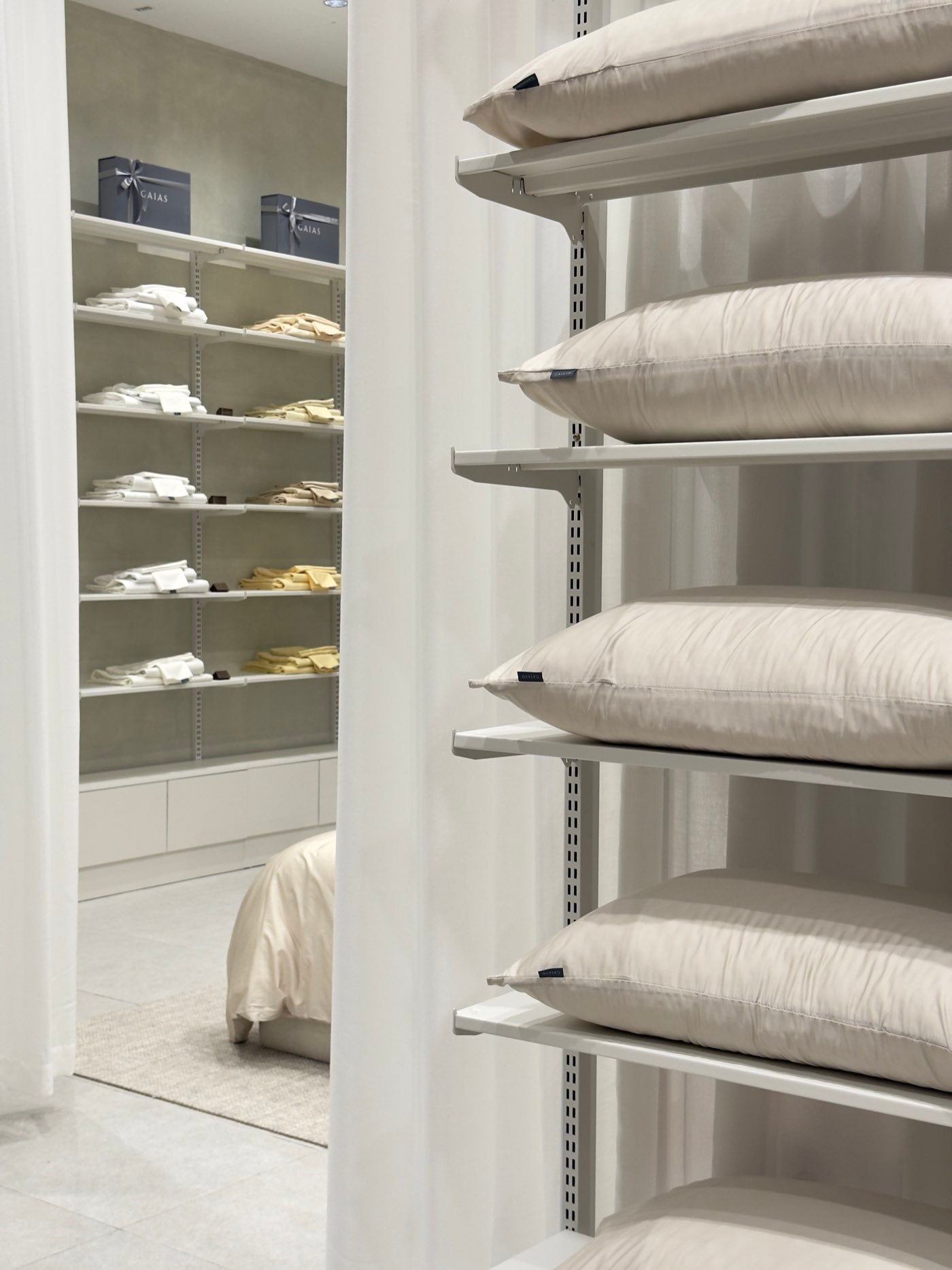 Pillow shelves and folded whites, with the made bed behind the curtain