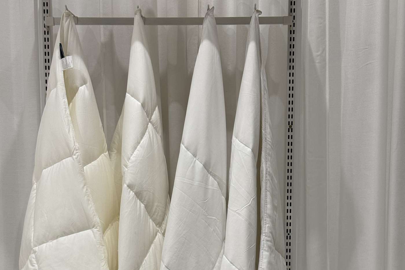 Quilted duvets hanging from a rail against a voile curtain