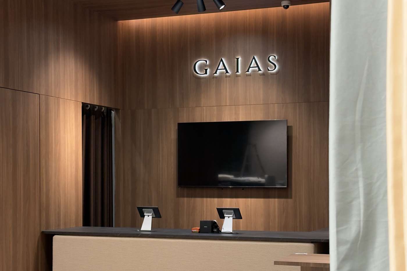 The GAIAS wordmark on a walnut reception wall above the counter