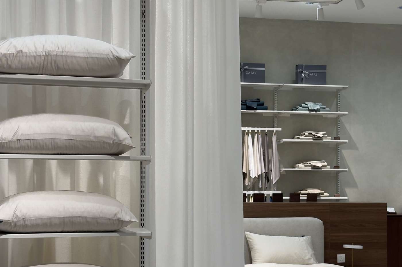 Pillows stacked on open shelves, with a made bed through the curtain