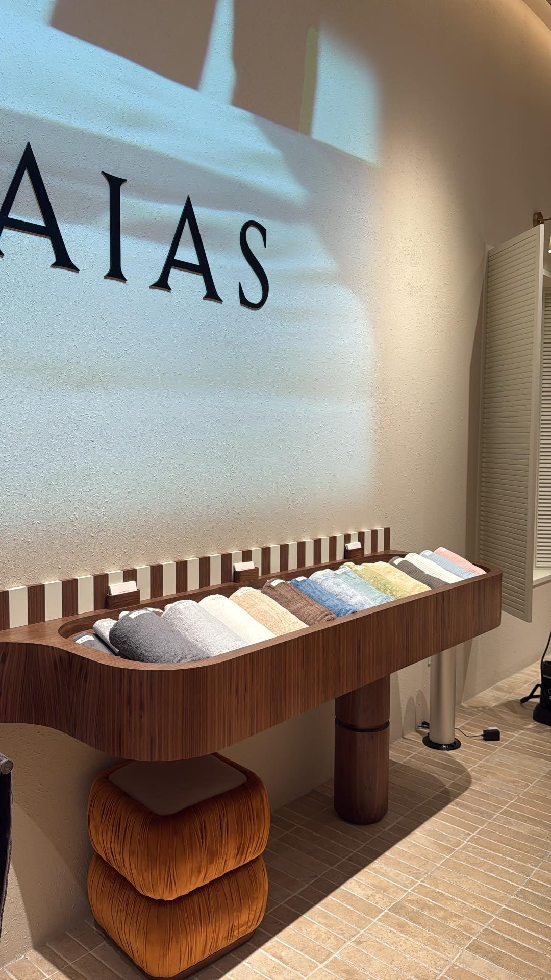The wordmark washed by moving light above a walnut console of folded textiles