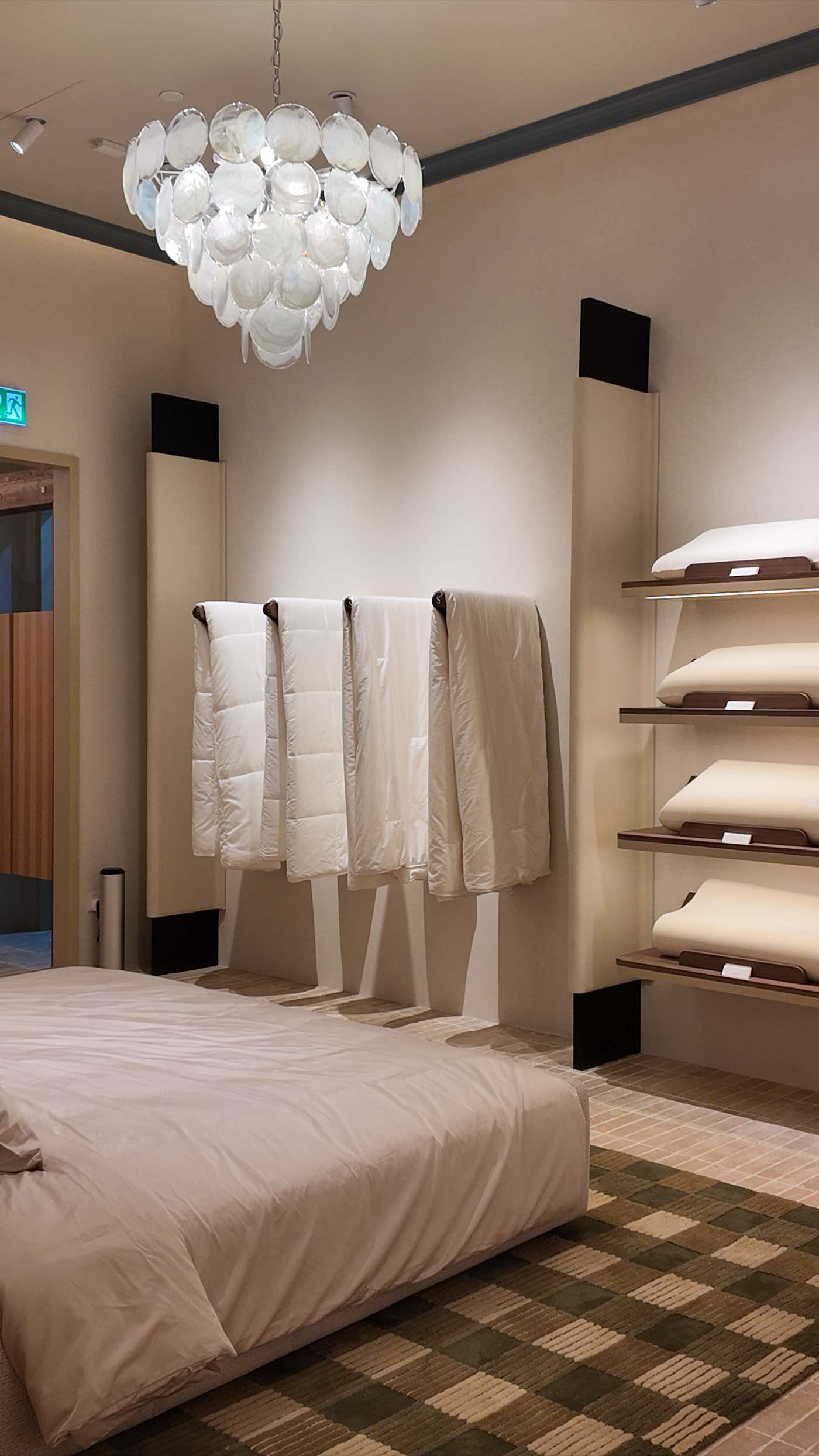 The bedroom at the back of the store — duvets on a rail and pillow shelves under the glass-disc chandelier
