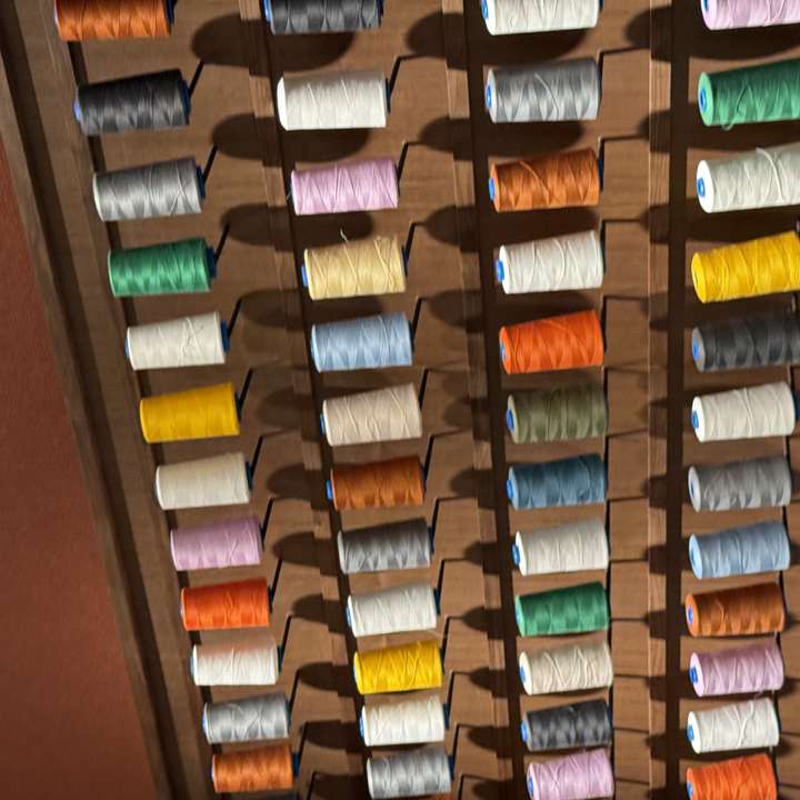 A wall of coloured thread spools on a timber lattice